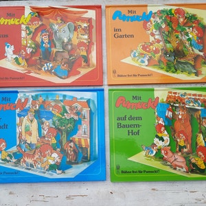 Op de afbeelding: Vier kleurrijke kinderboeken met de titel "Mit Pumuckl" en verschillende scènes. De boeken zijn allemaal even groot en hebben een vergelijkbaar ontwerp. De omslagen tonen illustraties van het personage Pumuckl in verschillende omgevingen, waaronder een circus, een tuin, een stad en een boerderij.
