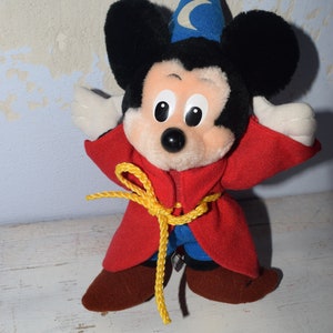 Könnte beinhalten: Ein Plüsch-Mickey-Mouse-Spielzeug, das eine rote Robe mit einem gelben Seilgürtel und einen blauen Zaubererhut mit einem Halbmond und einem Stern trägt.