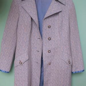 Può includere: Un lungo cappotto blu chiaro con un motivo geometrico bianco e blu chiaro. Il cappotto ha un colletto, maniche lunghe e una chiusura con bottoni.