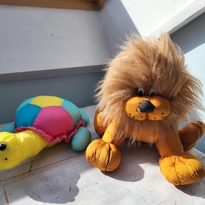 May include: A yellow and blue stuffed turtle with a pink and white shell and a brown stuffed lion with a long mane.