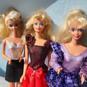 May include: Three blonde Barbie dolls wearing different outfits. The doll on the left is wearing a silver iridescent top and a black skirt. The doll in the middle is wearing a red and black sequined top with a red skirt. The doll on the right is wearing a purple top with a black and purple skirt.