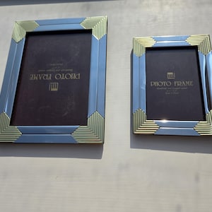 May include: Two rectangular photo frames with a metallic finish, featuring alternating smooth silver-toned panels and textured gold-toned corner accents. Each frame contains a dark brown insert with the text PHOTO FRAME printed in gold lettering.