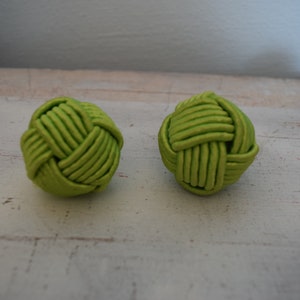 Könnte beinhalten: Zwei grüne, geknüpfte Kugeln aus Stoff. Die Kugeln liegen auf einer weißen Holzoberfläche.
