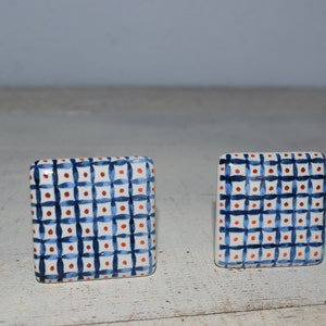 Könnte beinhalten: Zwei quadratische Keramik-Schubladengriffe mit weißem Hintergrund und einem blau-roten Karomuster.