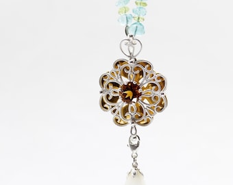 Peut inclure: Un collier en argent avec un pendentif floral délicat orné d'une pierre précieuse brune. Le collier est composé de perles bleu clair et vertes.
