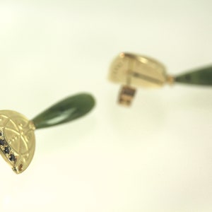 Peut inclure: Une paire de boucles d'oreilles en or avec une pierre de jade verte et des accents de diamants noirs. Les boucles d'oreilles sont en forme de goutte d'eau avec un motif d&eacute;coratif.