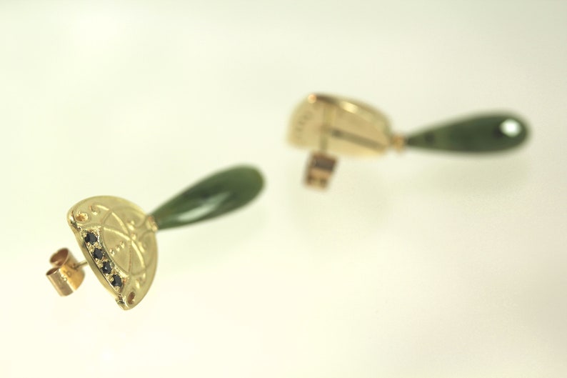 Peut inclure: Une paire de boucles d'oreilles en or avec une pierre de jade verte et des accents de diamants noirs. Les boucles d'oreilles sont en forme de goutte d'eau avec un motif d&eacute;coratif.