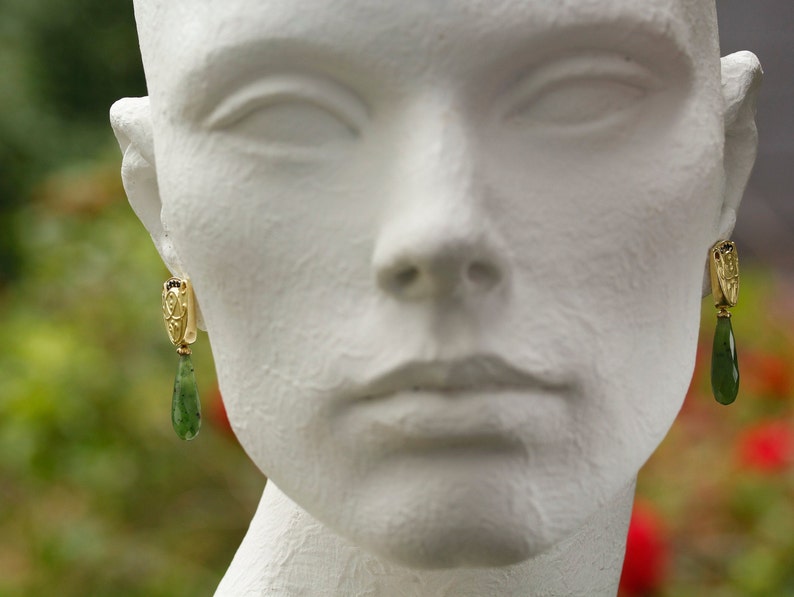 Peut inclure: Un mannequin blanc portant une paire de boucles d'oreilles en or avec des gouttes de pierres pr&eacute;cieuses vertes.
