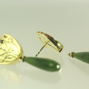 Peut inclure: Une paire de boucles d'oreilles en or avec une goutte de jade vert et un pendentif en or orn&eacute; de pierres noires. Le pendentif pr&eacute;sente un motif d&eacute;coratif.