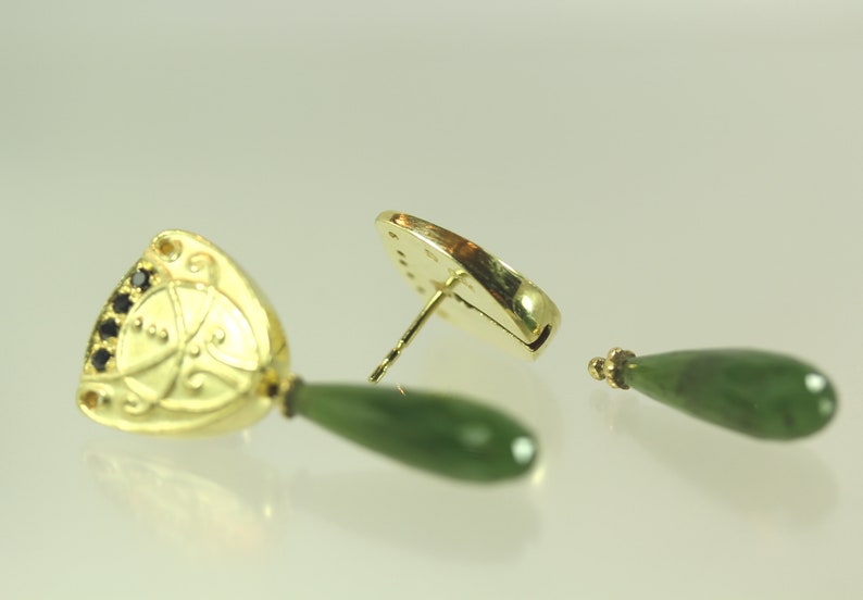Peut inclure: Une paire de boucles d'oreilles en or avec une goutte de jade vert et un pendentif en or orn&eacute; de pierres noires. Le pendentif pr&eacute;sente un motif d&eacute;coratif.
