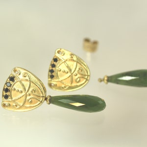 Peut inclure: Une paire de boucles d'oreilles en or avec des pierres pr&eacute;cieuses noires et des gouttes de jade vert. Les boucles d'oreilles pr&eacute;sentent un design d&eacute;taill&eacute; avec des motifs complexes.