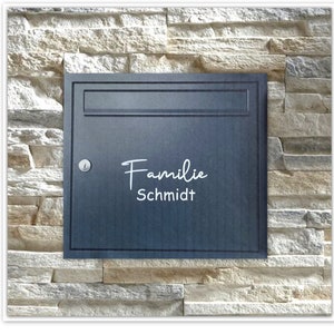 Könnte beinhalten: Ein dunkelgrauer Metallbriefkasten mit einer weißen Aufschrift "Familie Schmidt".