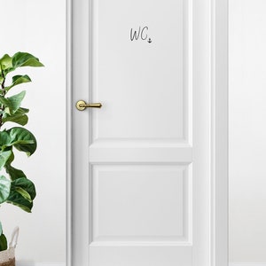 May include: White door with a gold door handle and a black handwritten sign that says "WC" with an anchor symbol.
