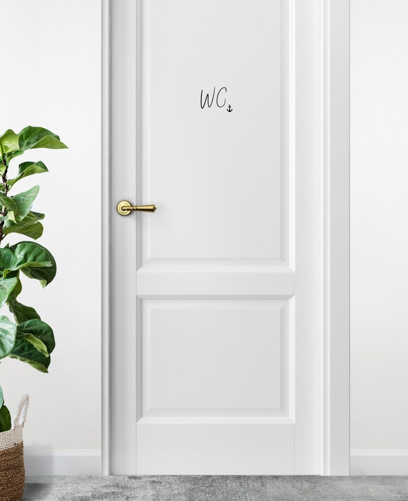 May include: White door with a gold door handle and a black handwritten sign that says "WC" with an anchor symbol.