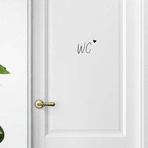 May include: White door with a gold door handle and a black handwritten sign that says "WC" with a small black heart next to it.