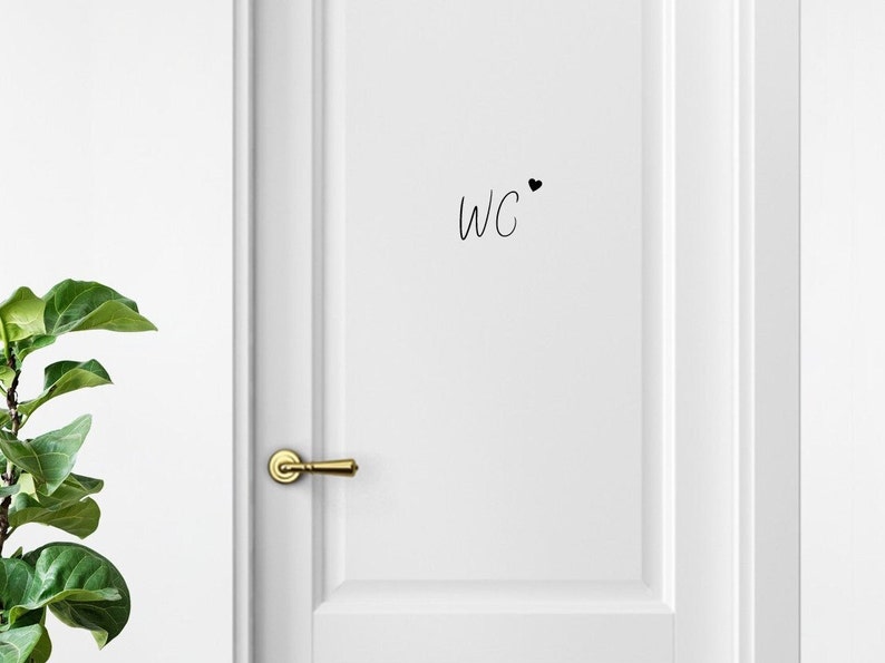 May include: White door with a gold door handle and a black handwritten sign that says "WC" with a small black heart next to it.