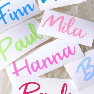 Könnte beinhalten: Eine Sammlung bunter Vinyl-Aufkleber mit Namen in Kursivschrift. Die Namen sind Finn, Paul, Mila, Hanna und Pauline. Die Aufkleber befinden sich auf einem weißen Hintergrund.