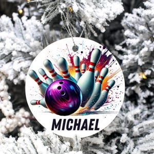 May include: A round Christmas ornament featuring a bowling scene with a purple bowling ball and white bowling pins with red stripes. The name "MICHAEL" is printed in bold black letters at the bottom.