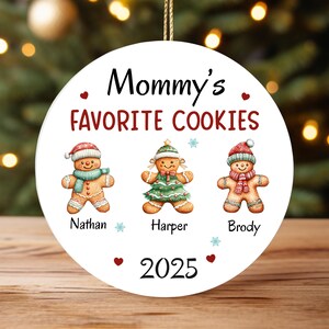 May include: A white, round Christmas ornament with the text "Mommy's Favorite Cookies" in red and black. It features gingerbread people with names: Nathan, Harper, and Brody, and the year 2025.