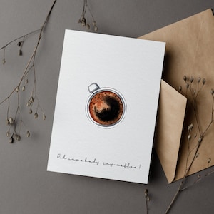 Könnte beinhalten: Eine weiße Karte mit einer Aquarellillustration einer Kaffeetasse, von oben gesehen, mit dem Text "Did somebody say coffee?" in einer handschriftlichen Schriftart. Die Karte liegt neben einem braunen Umschlag und Zweigen getrockneter Pflanzen.