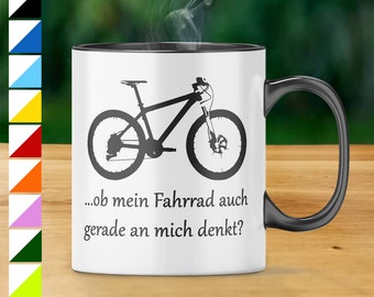 Puede incluir: Taza de cerámica blanca con borde y asa negros. La taza presenta una silueta negra de una bicicleta de montaña y el texto "...ob mein Fahrrad auch gerade an mich denkt?"