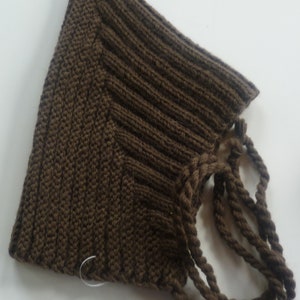 Puede incluir: Un gorro de punto marrón con un cordón largo y grueso. El gorro tiene una parte superior puntiaguda y una textura acanalada.