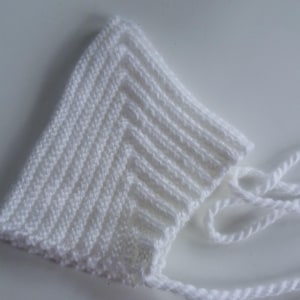 Könnte beinhalten: Weißer gestrickter Baby-Mützchen mit gebundenem Band.