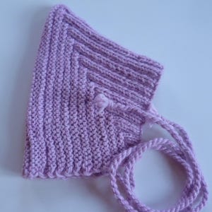 Puede incluir: Un gorro de bebé tejido de color lila claro con un diseño texturizado. El gorro tiene una parte superior redondeada y una correa para la barbilla hecha con el mismo hilo. El gorro está hecho de un hilo suave y texturizado.
