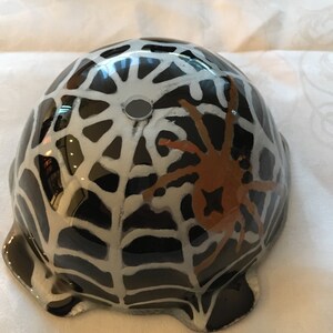 May include: Black ceramic bowl with a white spiderweb design and a brown spider in the center. The bowl has a hole in the top.