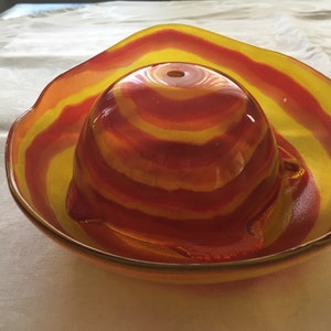 Op de afbeelding: Een rode en gele gestreepte glazen kom met een kleinere, bijpassende kom erin. De kommen zijn gemaakt van helder glas met een draaiend patroon van rood en geel.