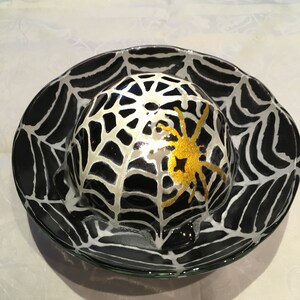 May include: A black glass bowl with a white spiderweb design and a gold spider in the center. The bowl is perfect for serving snacks or desserts.