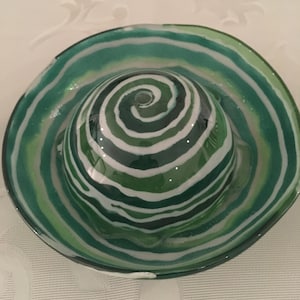 Op de afbeelding: Een groene en witte glazen kom met een swirl-patroon. De kom heeft een klein gaatje in het midden.