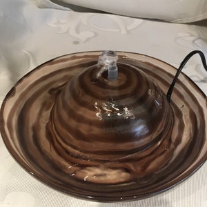 Op de afbeelding: Een bruine en witte keramische dierenfontein met een swirl-patroon. De fontein heeft een heldere plastic pomp en een snoer.