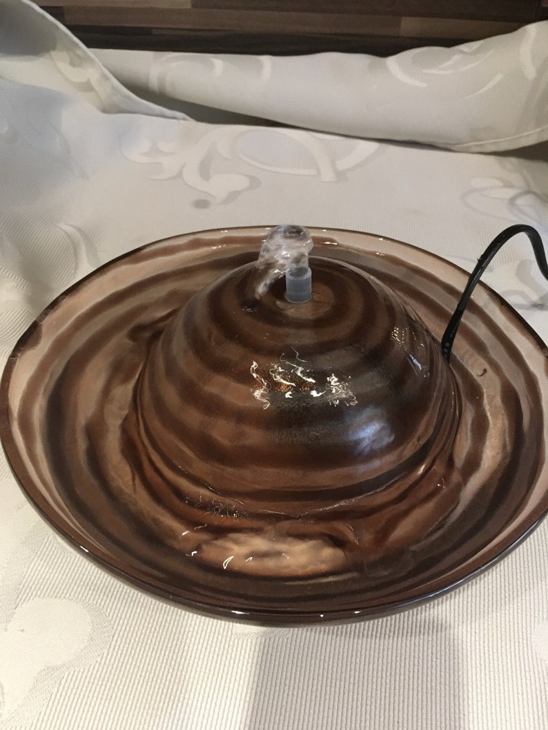 Op de afbeelding: Een bruine en witte keramische dierenfontein met een swirl-patroon. De fontein heeft een heldere plastic pomp en een snoer.