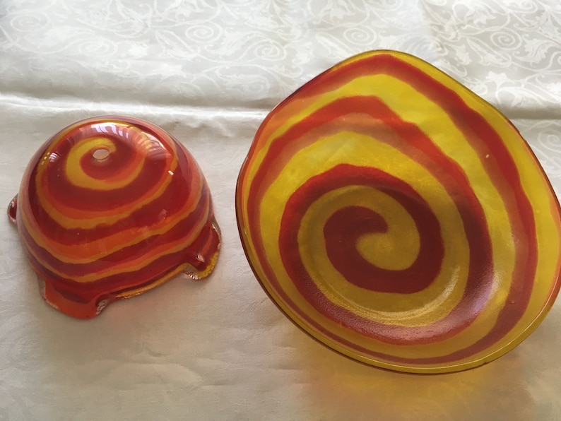 Op de afbeelding: Twee glazen kommen met een rood en geel swirl-patroon. De kommen zijn gemaakt van helder glas en hebben een glanzende afwerking.