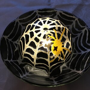 May include: A black and white glass dome with a spider web design and a gold spider inside. The dome is lit from within, creating a glowing effect.