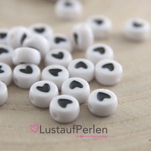 May include: White heart-shaped beads with black hearts. The beads are approximately 1 cm in diameter.