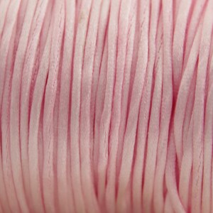 May include: Close-up of a spool of pink satin cord. The cord is tightly wound and has a smooth, silky texture.
