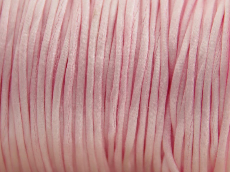 May include: Close-up of a spool of pink satin cord. The cord is tightly wound and has a smooth, silky texture.