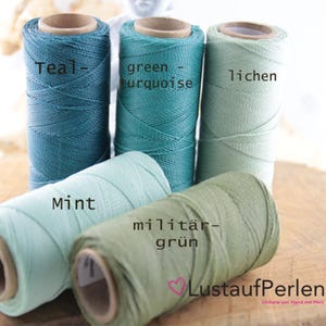 Könnte beinhalten: Fünf Spulen gewachster Baumwollschnur in Grüntönen, Türkis und Mint. Die Spulen sind mit den Farben beschriftet: Teal, grün-türkis, Flechte, Minze und Militärgrün.