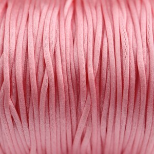 May include: Close-up of a spool of pink cord. The cord is made of a soft, woven material and is perfect for crafting projects.