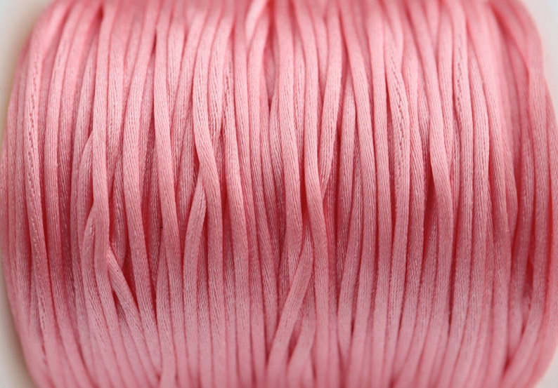 May include: Close-up of a spool of pink cord. The cord is made of a soft, woven material and is perfect for crafting projects.