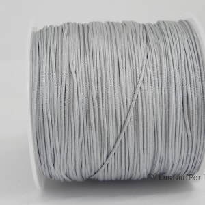 Könnte beinhalten: Eine Spule silbergrauer elastischer Kordel, perfekt für die Schmuckherstellung oder Bastelarbeiten.