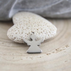 May include: A silver-toned metal angel charm featuring a smooth, polished surface with a small circular loop at the top for attachment. The charm has a simple, stylized silhouette with outstretched wings and a flared base, reflecting light.