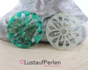 May include: Two round, decorative, floral-shaped, resin cabochons. One is green and white with a marbled effect. The other is white with a translucent, frosted look. Both have a raised, floral design.
