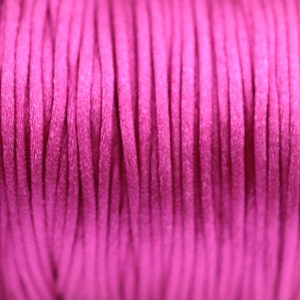 May include: Close-up of a spool of bright pink cord. The cord is made of a soft, smooth material and is perfect for crafting projects.
