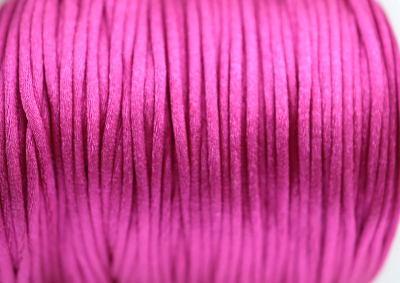 May include: Close-up of a spool of bright pink cord. The cord is made of a soft, smooth material and is perfect for crafting projects.
