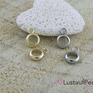 Könnte beinhalten: Drei Metall-Sprünge in Gold, Silber und Schwarz. Die Ringe sind rund und haben oben eine kleine Schlaufe. Sie sind auf einer hellbraunen, strukturierten Oberfläche angeordnet.