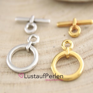 Könnte beinhalten: Zwei Sätze silberner und goldener Toggle-Verschlüsse mit einem runden Ring. Die Verschlüsse sind aus Metall und haben eine polierte Oberfläche.