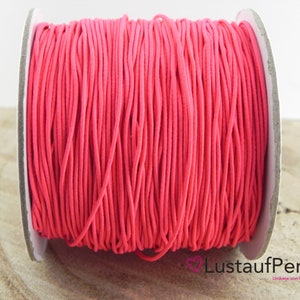 Könnte beinhalten: Eine Spule mit leuchtend pinkfarbenem Gummiband. Das Band ist eng um eine Pappspule gewickelt. Der Text "LustaufPerlen" ist auf der Spule zu sehen. Das Band scheint aus einem flexiblen Material zu bestehen, das für verschiedene Bastelprojekte geeignet ist.